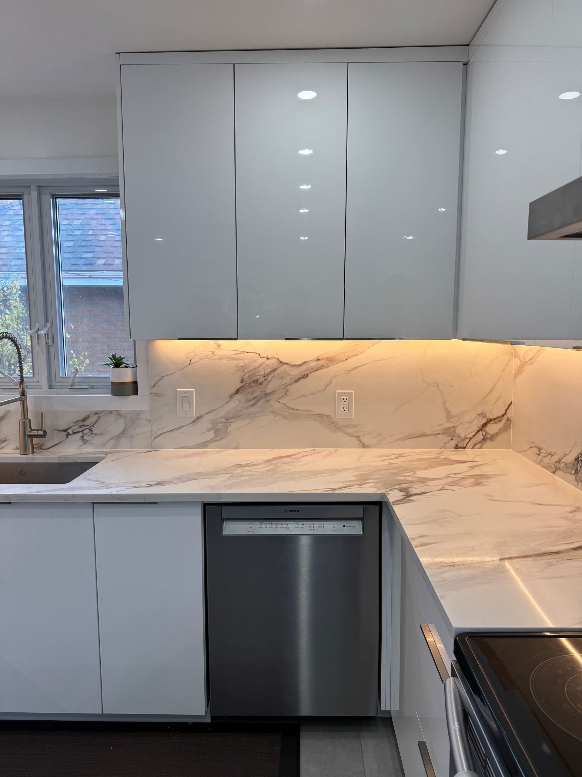 Une cuisine avec des armoires blanches, un lave-vaisselle en acier inoxydable, un évier et une fenêtre.