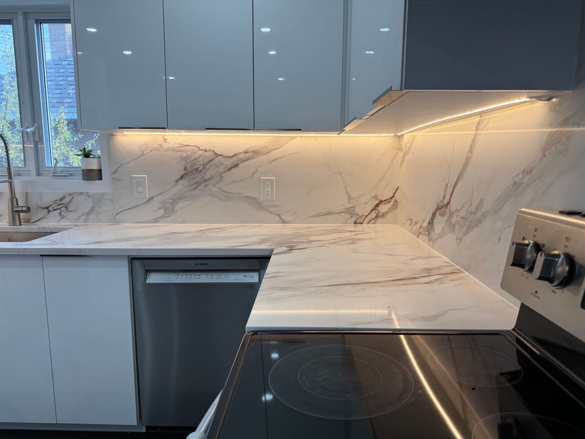 Une cuisine avec cuisinière, évier, lave-vaisselle et comptoirs en marbre.