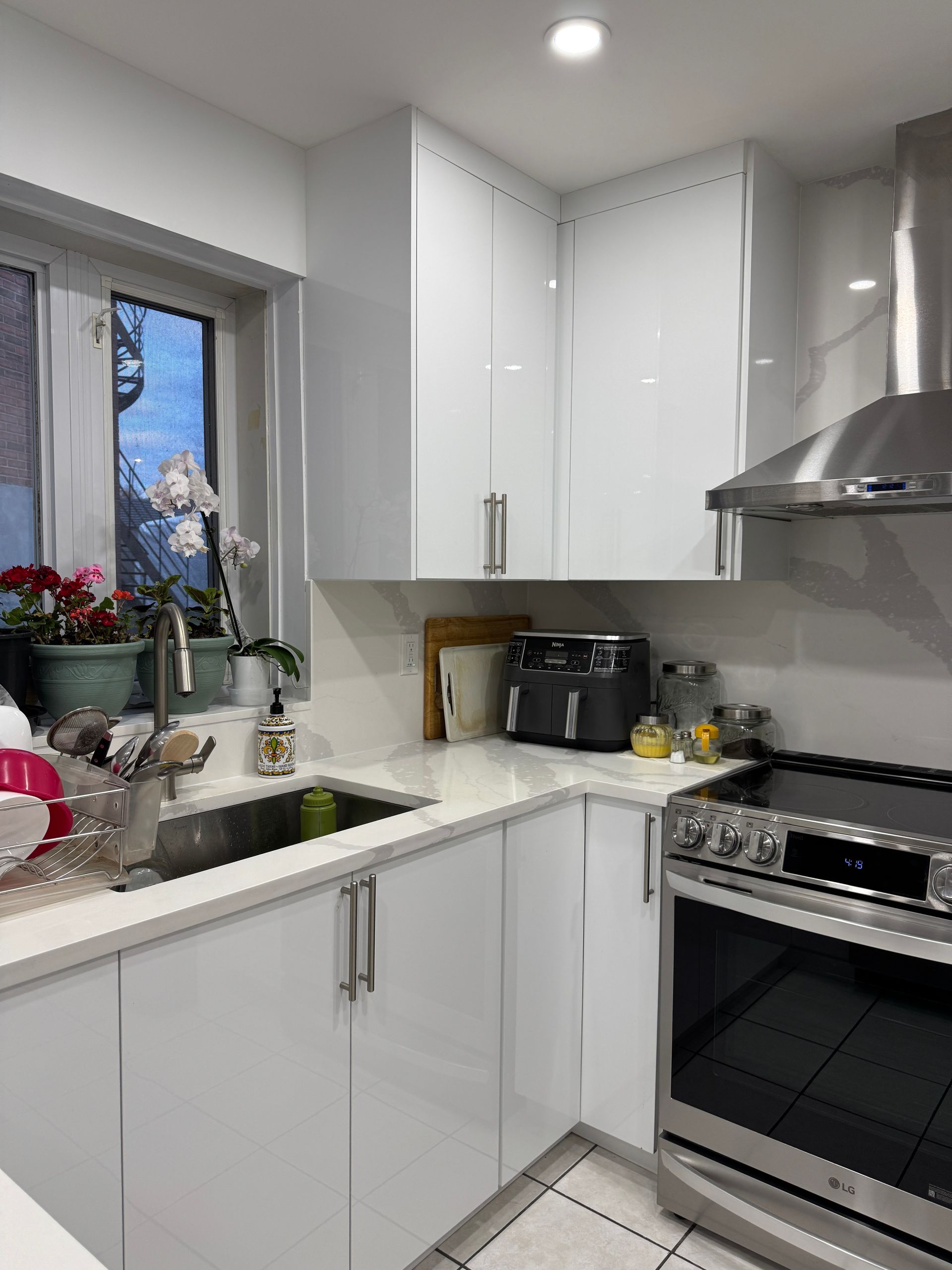 Une cuisine avec des armoires blanches, une cuisinière, un évier et une fenêtre.