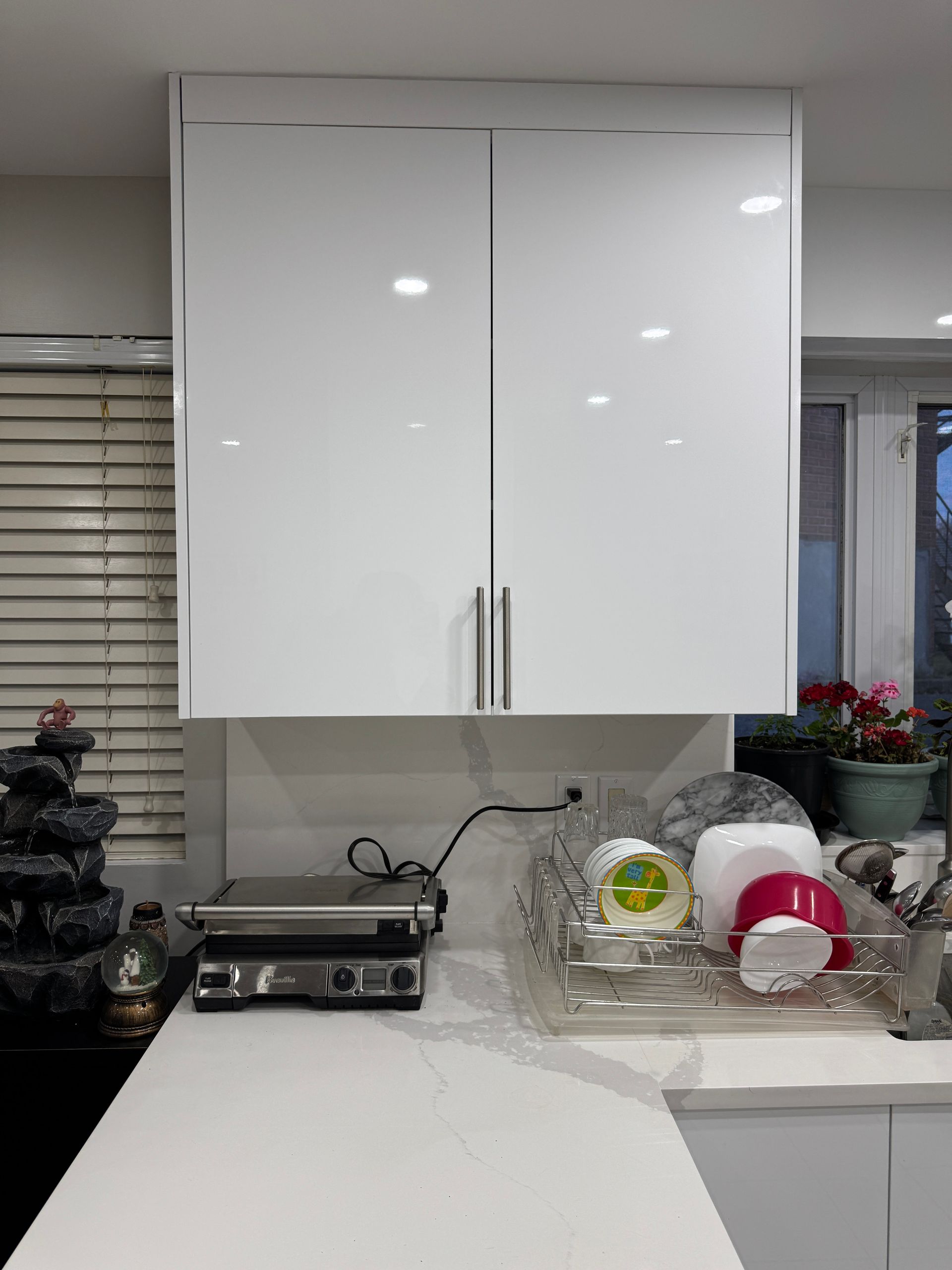 Une cuisine avec des armoires blanches, un évier, un gril et un égouttoir à vaisselle.