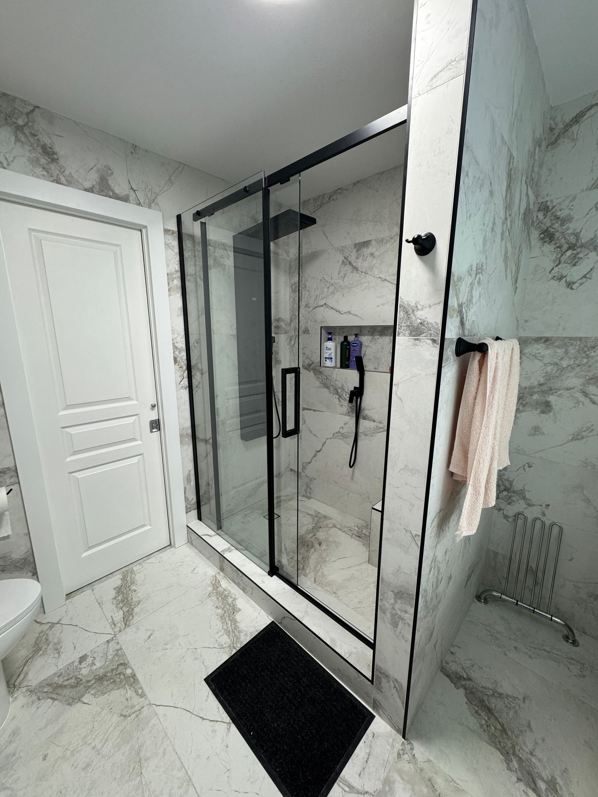 Une salle de bain avec une douche à l'italienne et un tapis noir au sol.