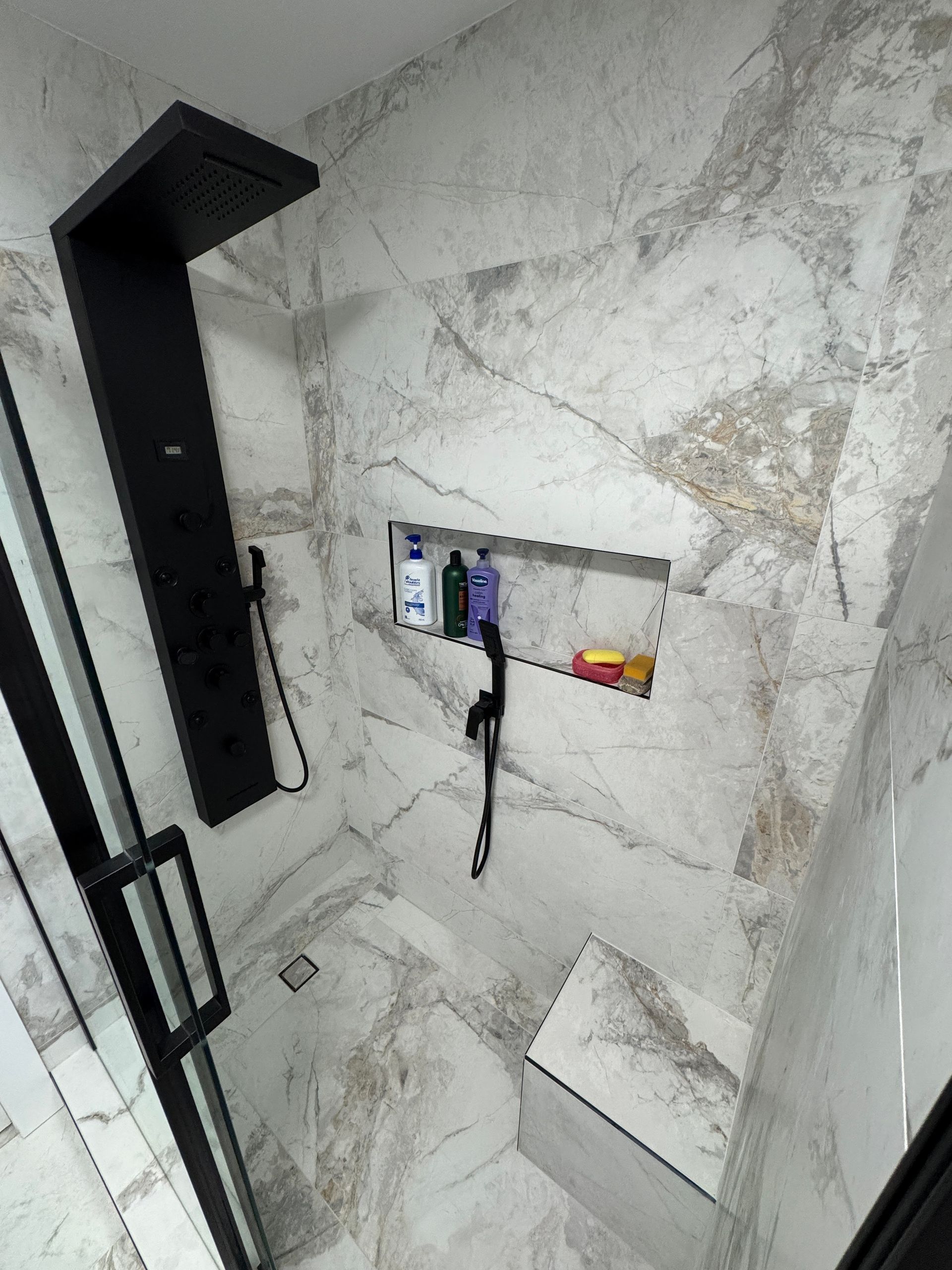 Une salle de bain avec une douche et une étagère avec des bouteilles dessus.