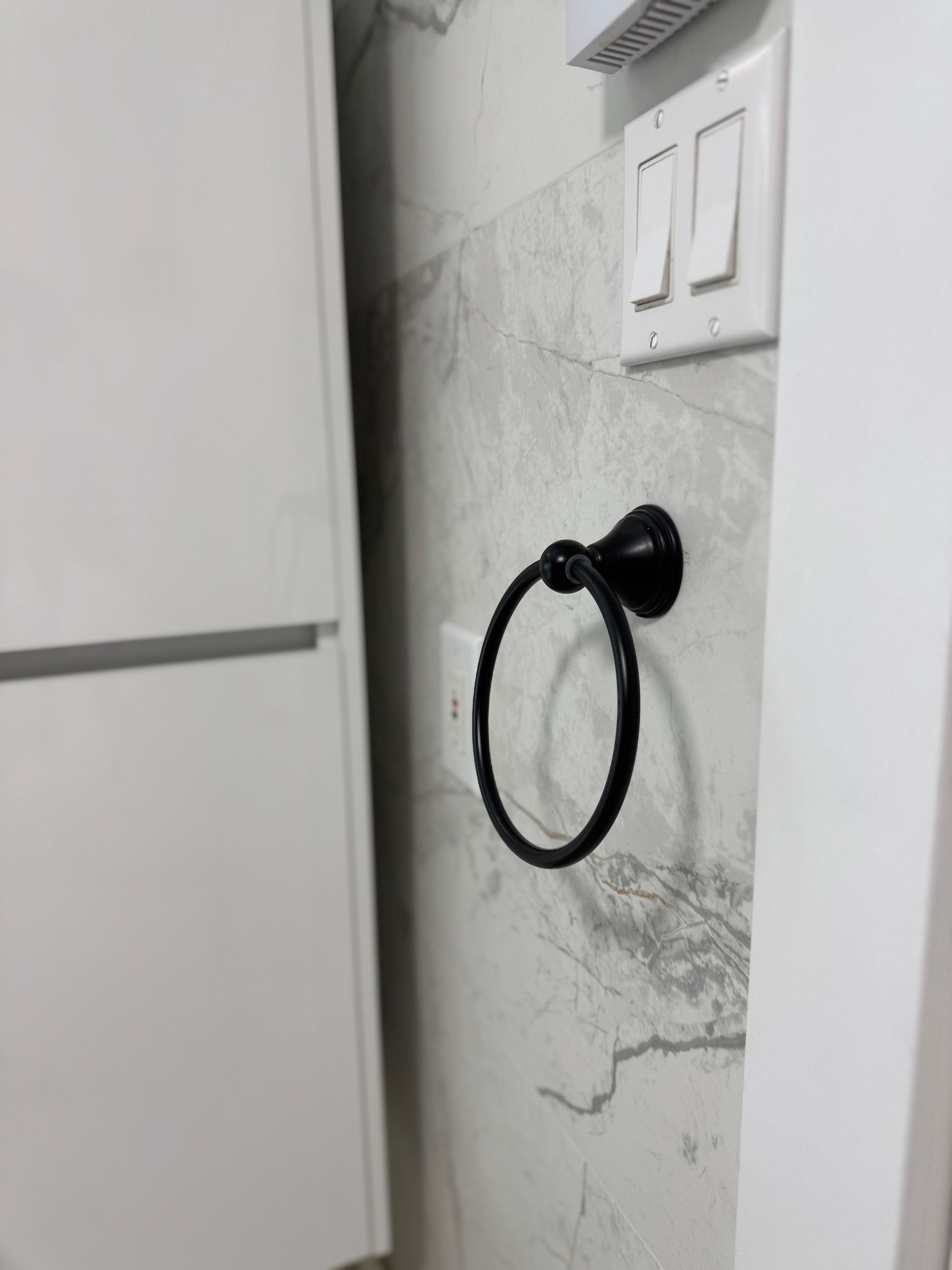 Un anneau porte-serviettes est accroché sur un mur blanc à côté d'un réfrigérateur.