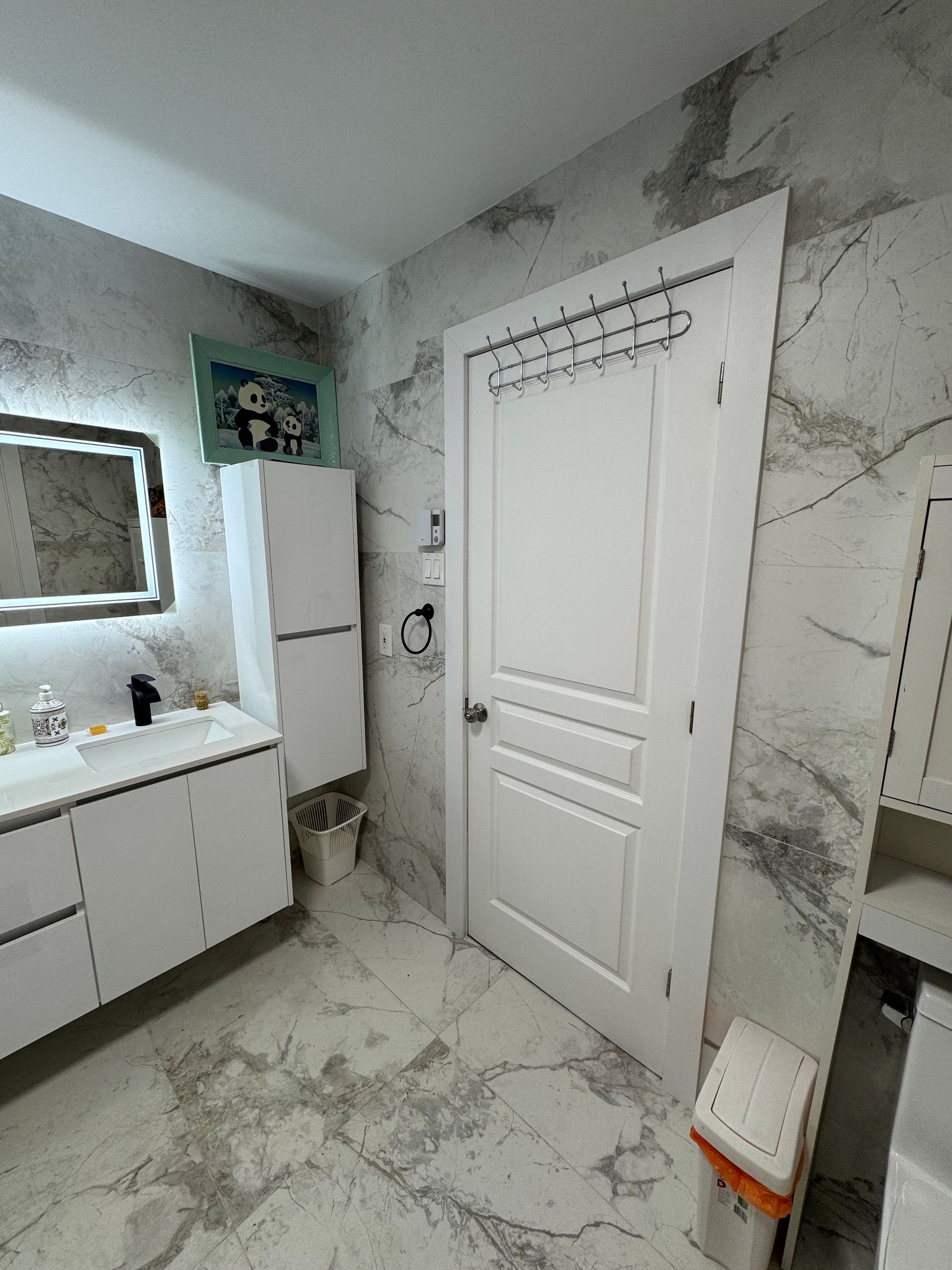 Une salle de bain avec des armoires blanches, un lavabo, un miroir et une poubelle.