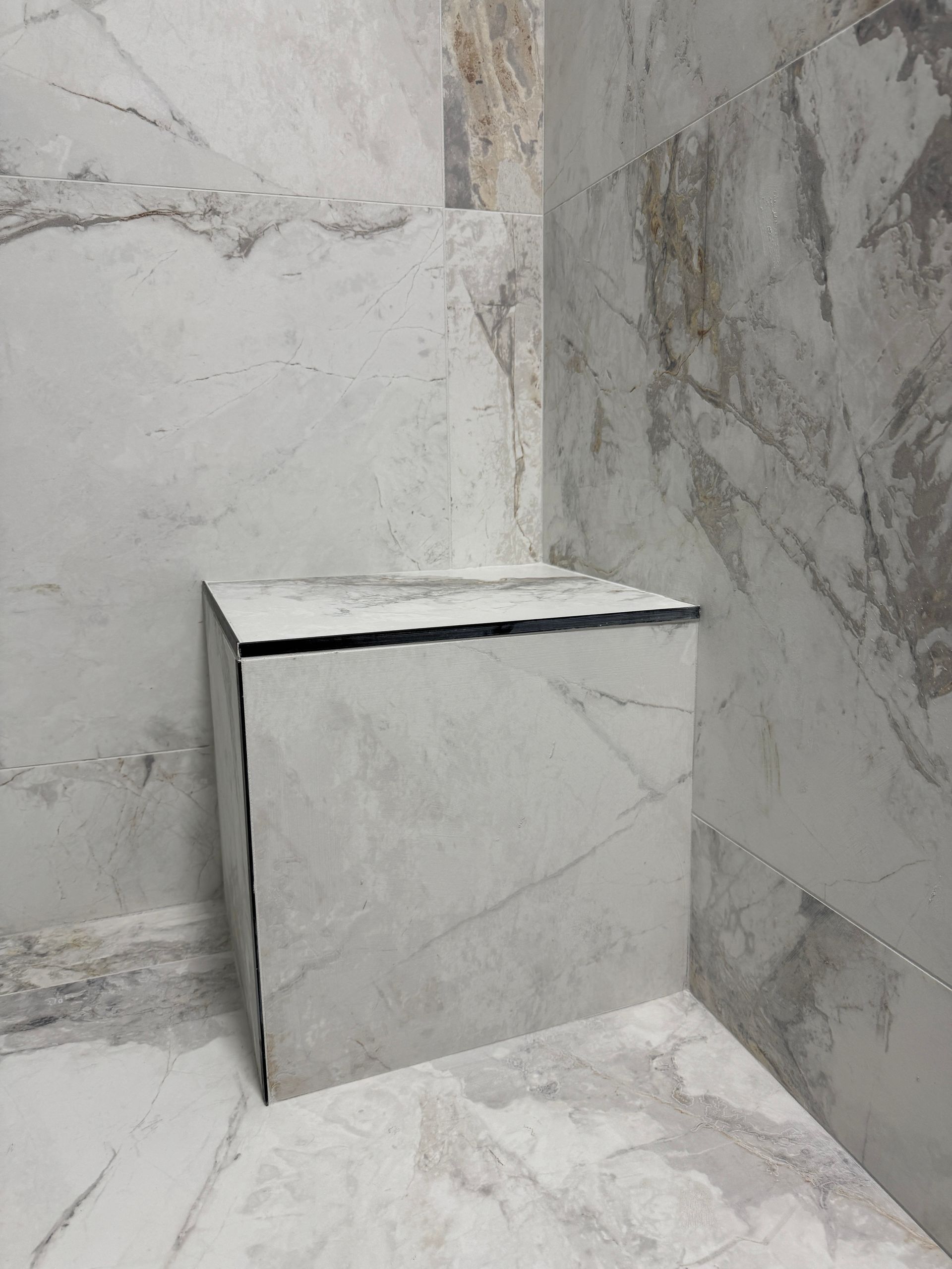 Un coin de salle de bain avec carrelage en marbre et siège de douche.