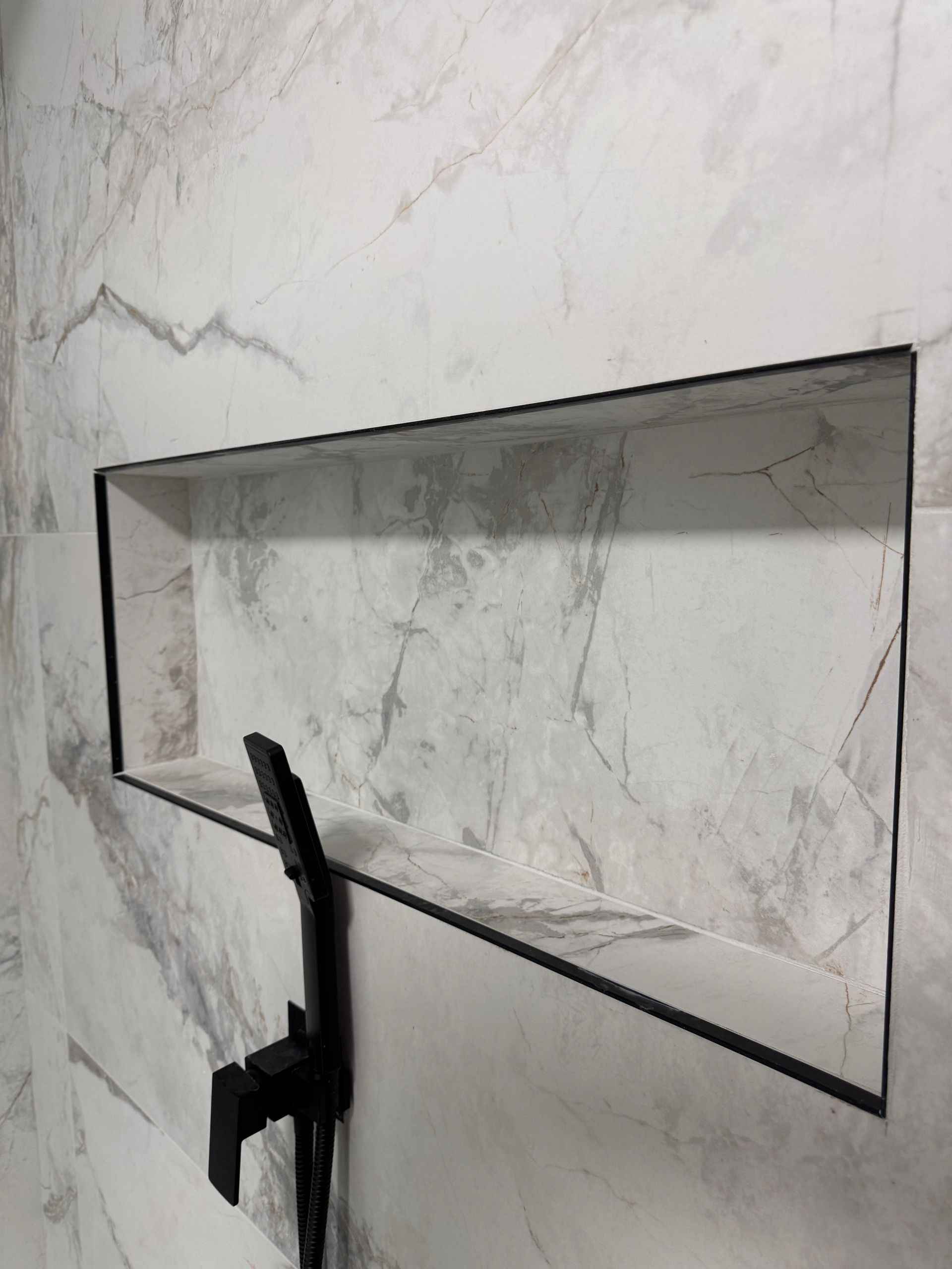 Une salle de bain avec une pomme de douche et une étagère dans le mur.