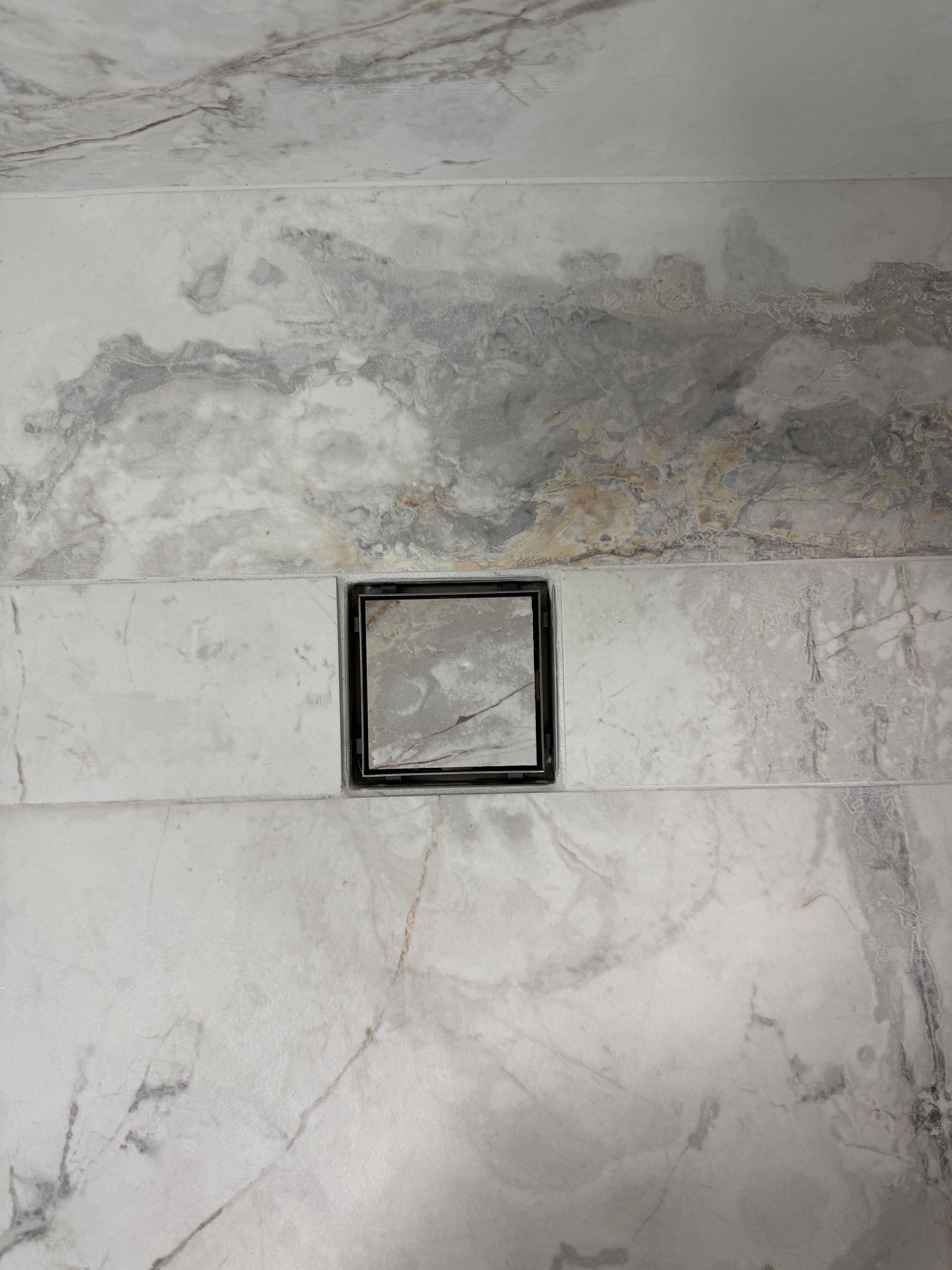 Un drain carré sur un sol en marbre dans une salle de bain.