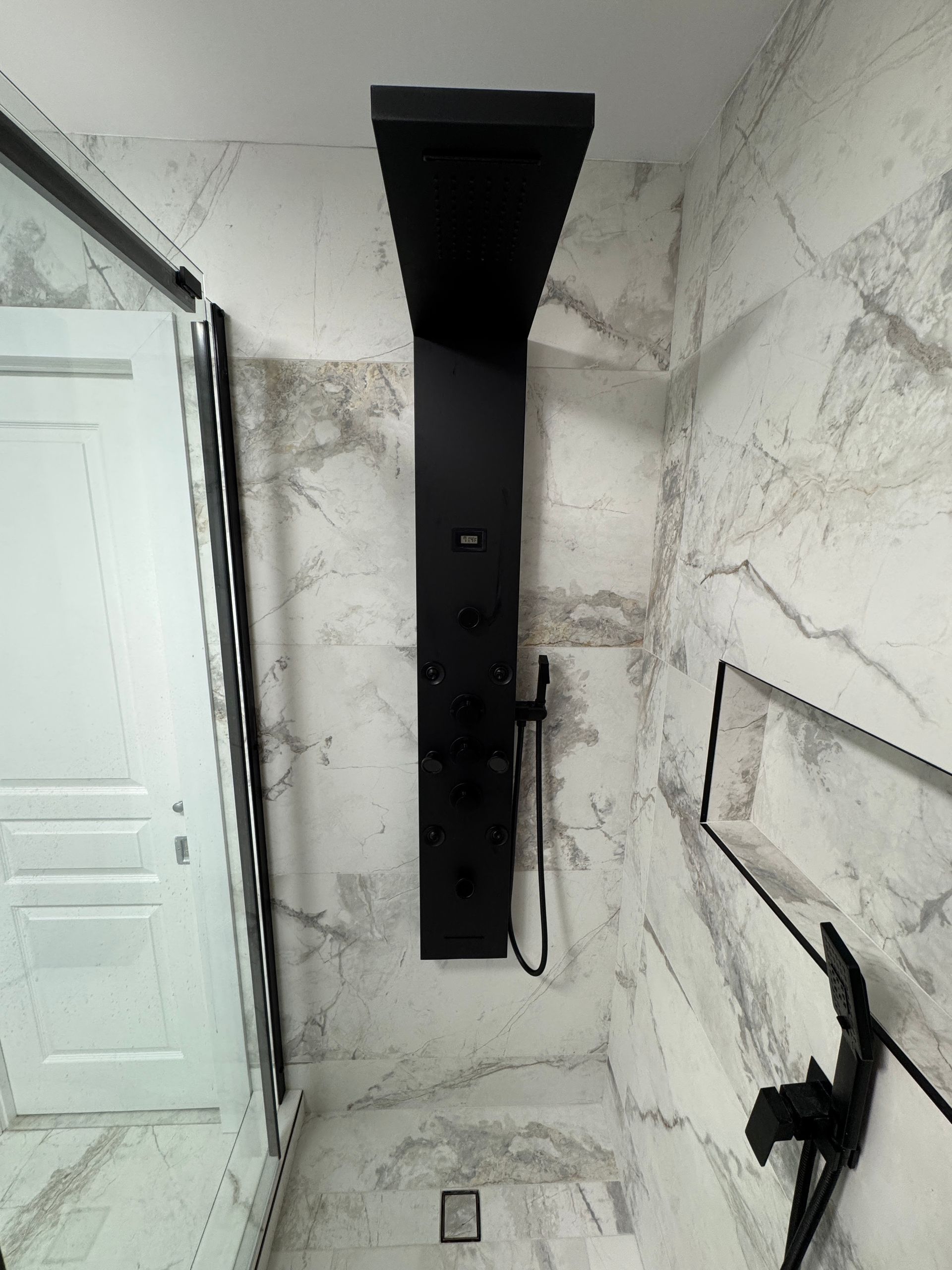 Une salle de bain avec des murs en marbre et une pomme de douche noire.