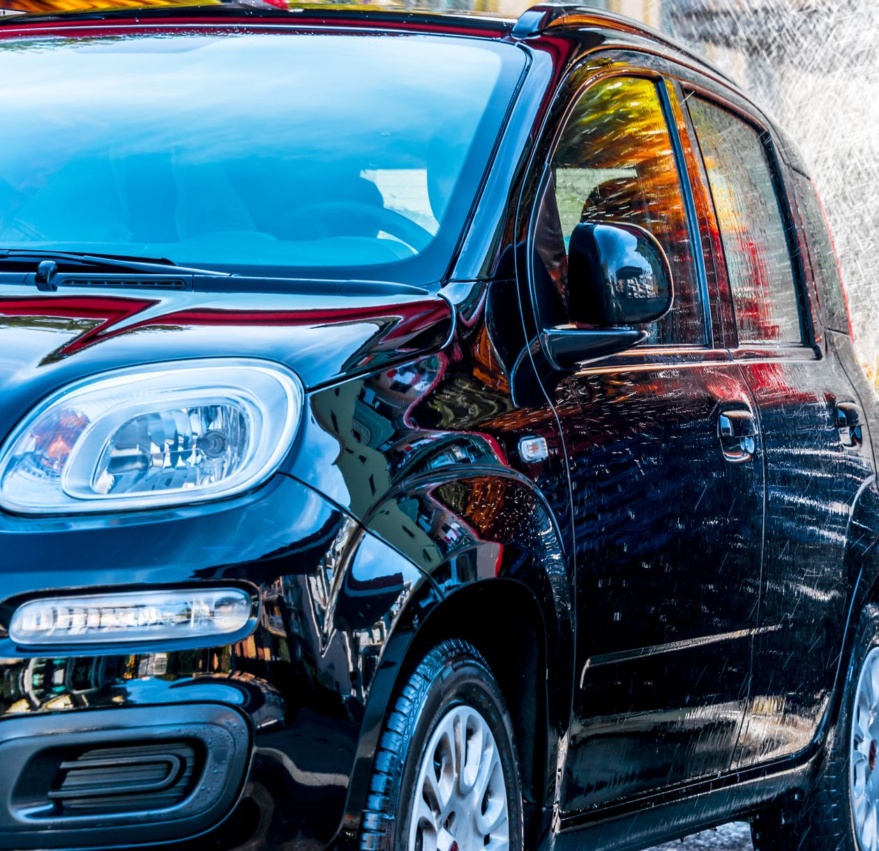 Blue car covered in white foam at a car wash, tire and front end visible.