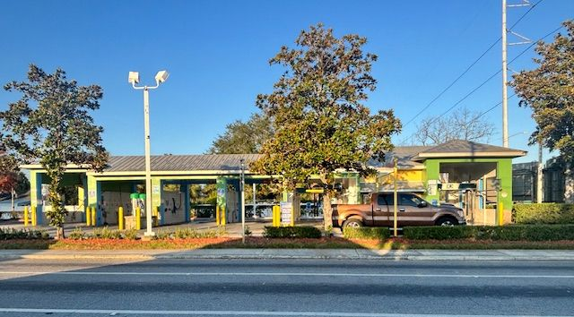 Black car in a car wash, surrounded by blue, red, and yellow rotating brushes and spraying water.