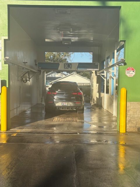 Red car inside a car wash, surrounded by yellow and black brushes, water spraying.