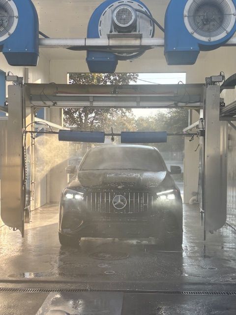 Car in a car wash, surrounded by blue brushes and spraying water, covered in foam.