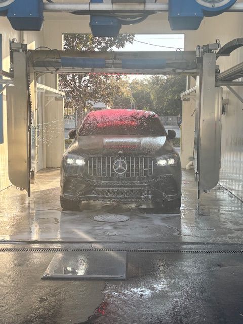 Silver car being washed in a carwash; water sprays, red brushes.