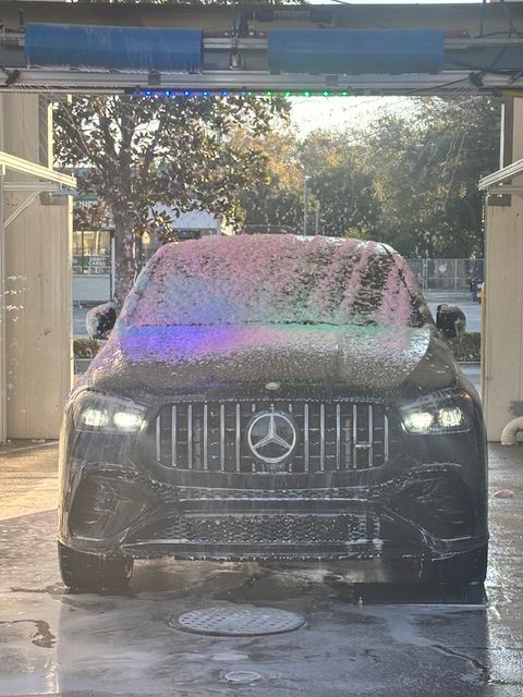 Silver SUV exiting car wash; blue bubble decor on the walls, sunlit.