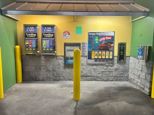 Silver car in a car wash, being sprayed with water and scrubbed by blue brushes.