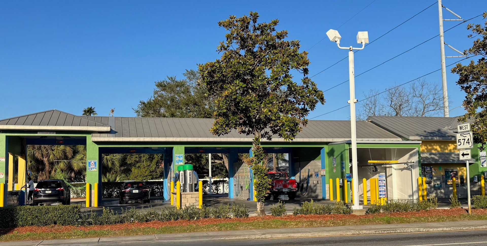 White car in a car wash, blue brushes are cleaning the vehicle.