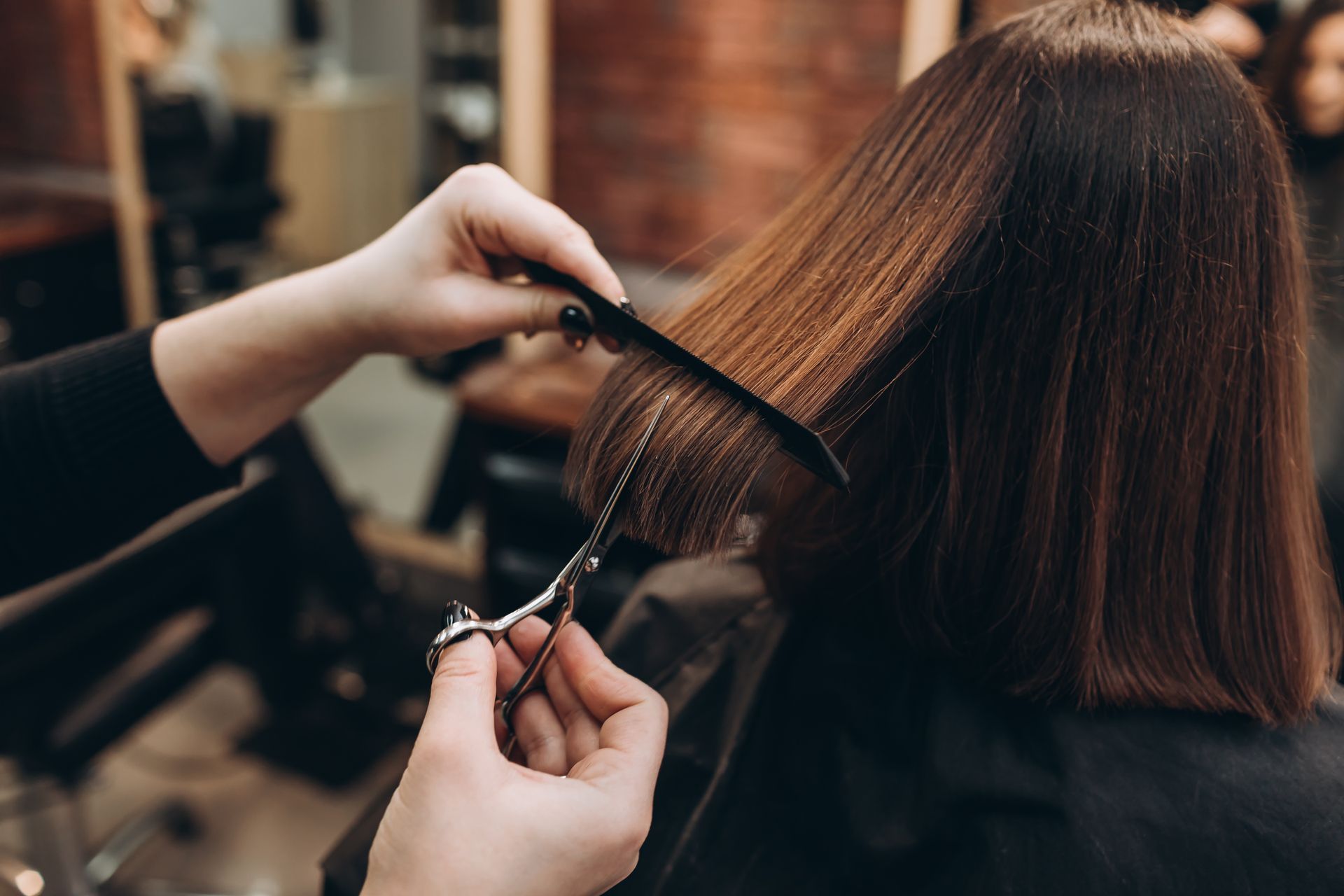 Hairdresser cutting straight brown hair in a salon with scissors and comb