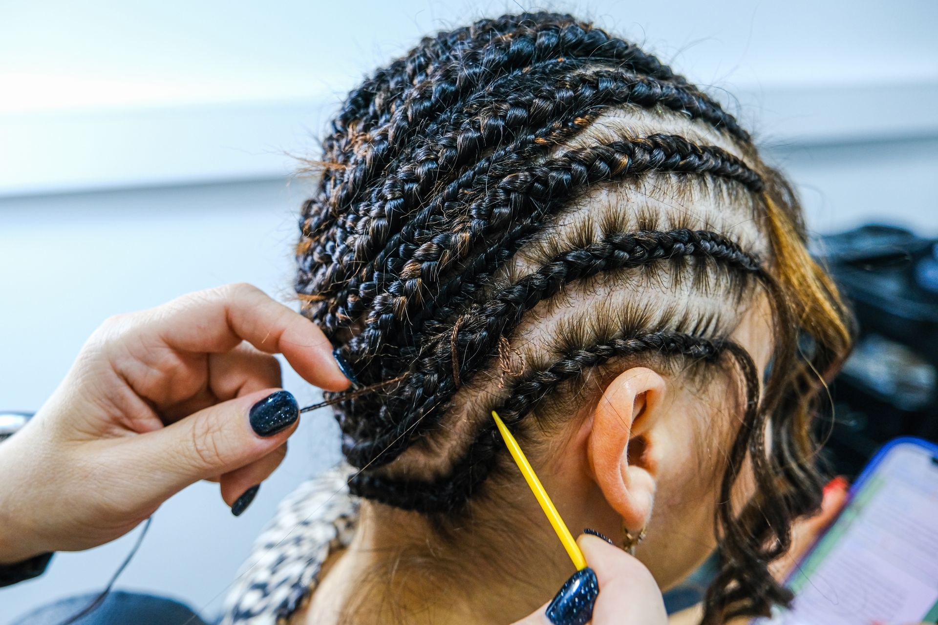 Hands braiding black hair with a yellow comb in a close-up salon scene