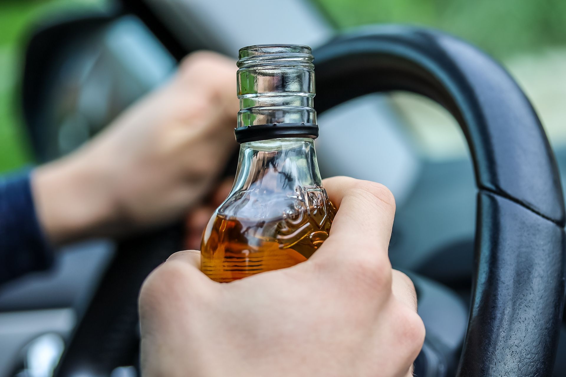 A person is holding a bottle of alcohol while driving a car.