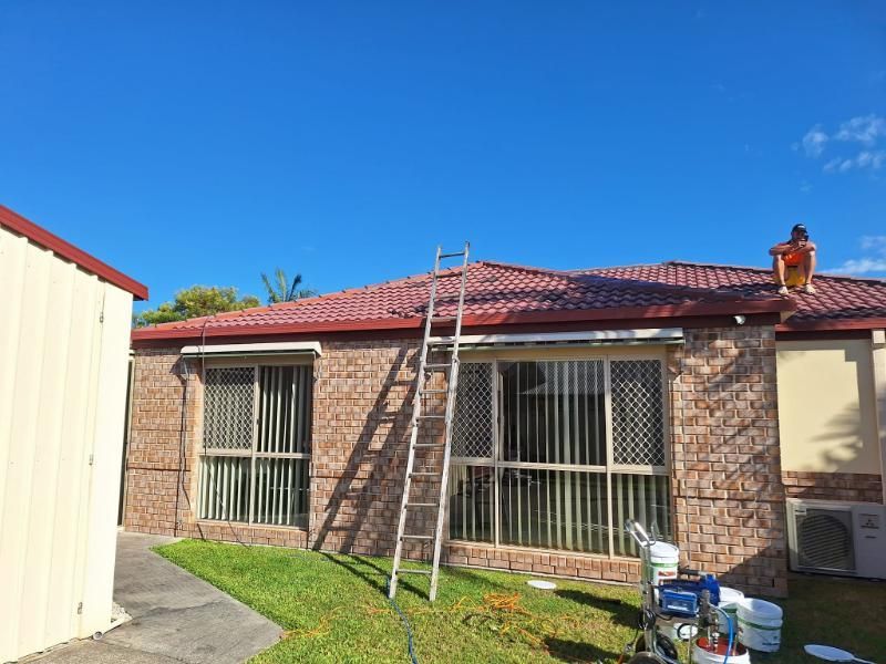 A Man is Painting the Roof of a House With a Ladder — Roofing Gold Coast in Tallebudgera, QLD
