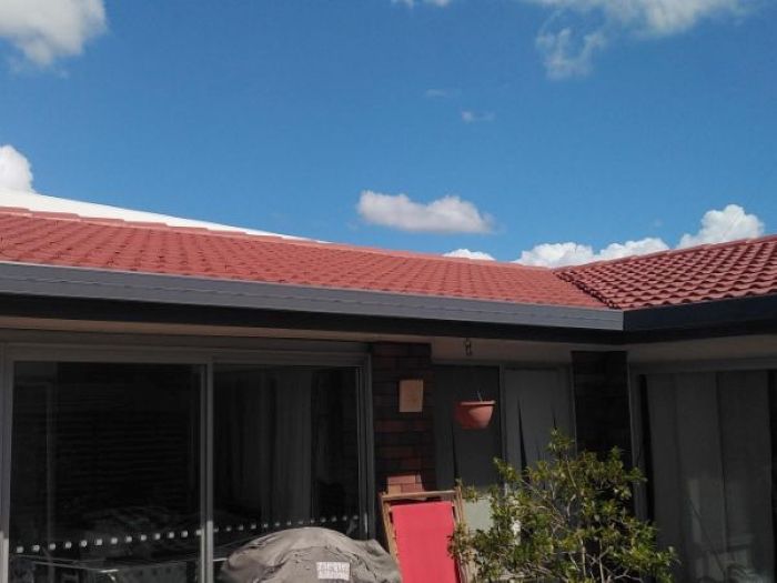 A House With a Red Tiled Roof and a Red Chair in Front of It — Roofing Gold Coast in Tallebudgera, QLD