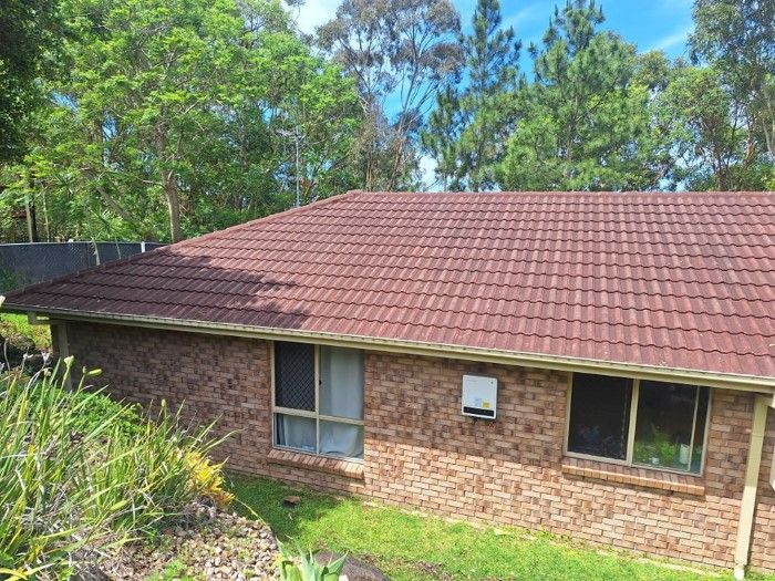 A Brick House With a Red Tiled Roof is Surrounded by Trees — Roofing Gold Coast in Tallebudgera, QLD