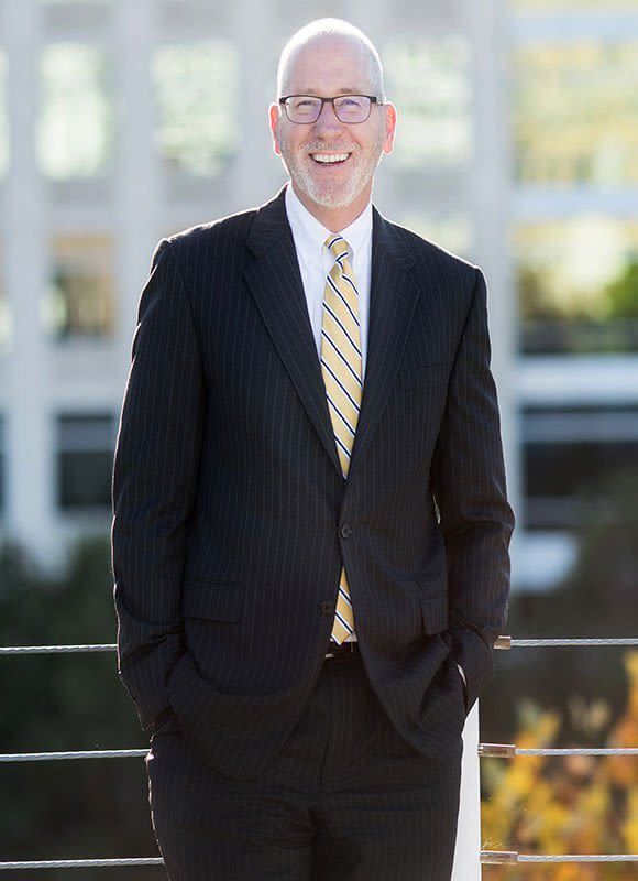 A man in a suit and tie is standing with his hands in his pockets.