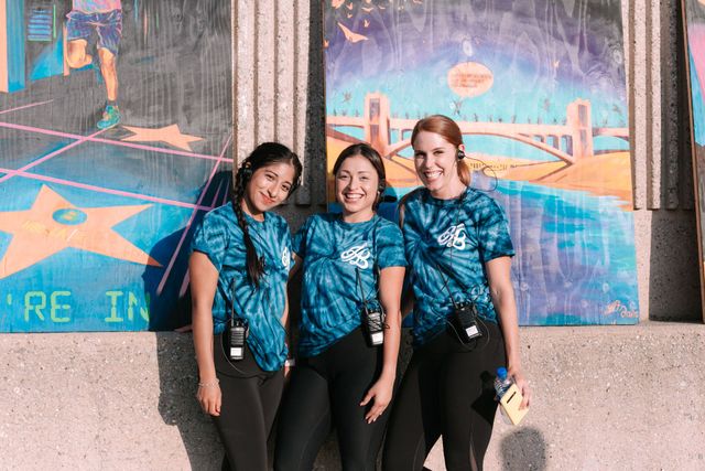 Three women are posing for a picture in front of a mural.