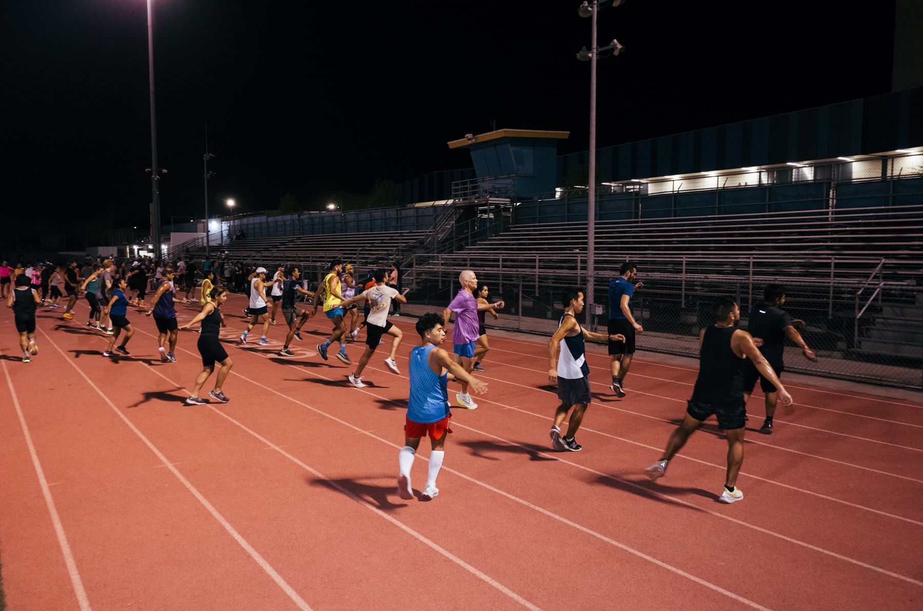 A group of people are running on a track at night.