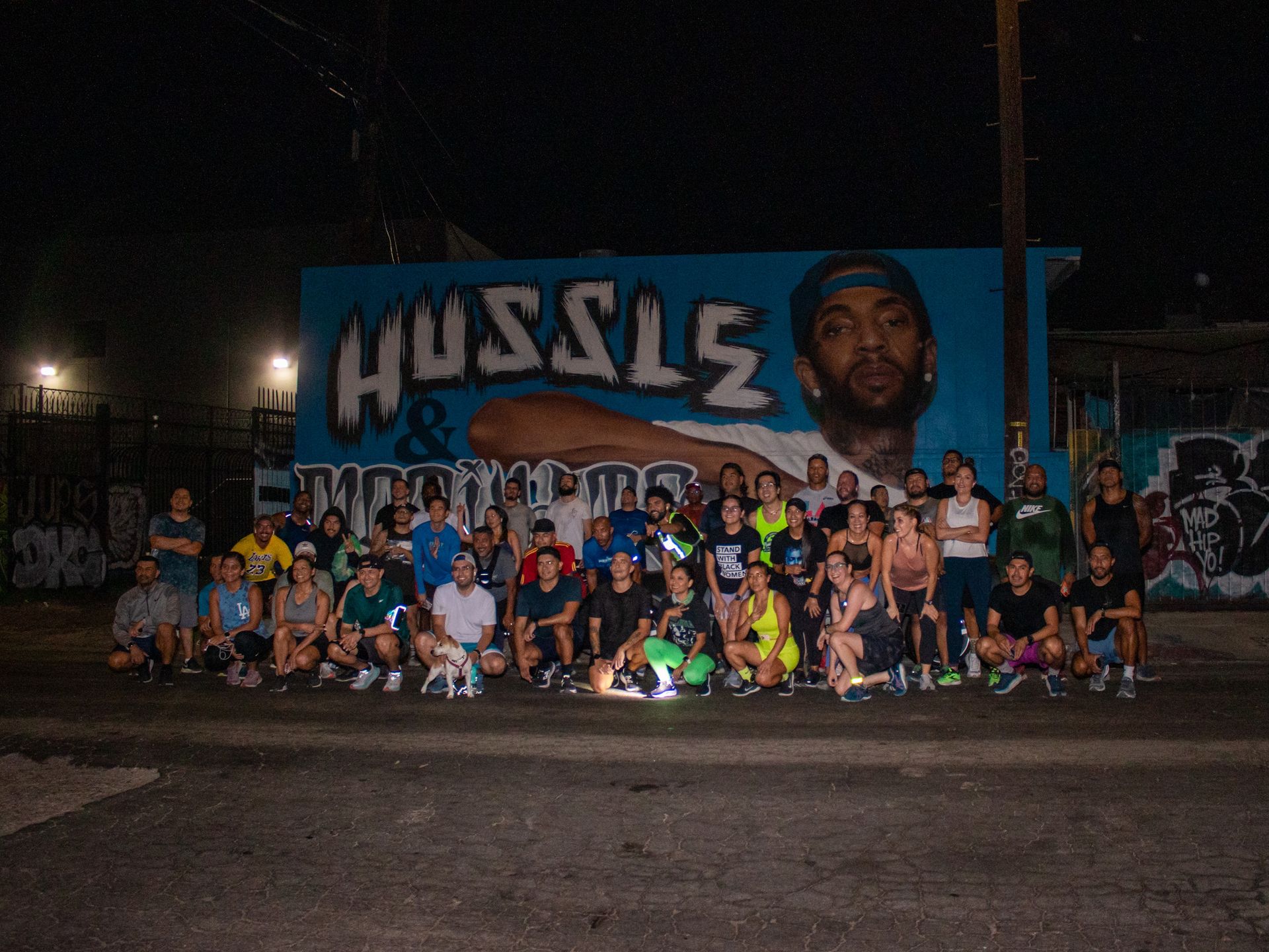 Large group of BlacklistLA runners posing in front of a street art mural featuring Nipsey Hussle