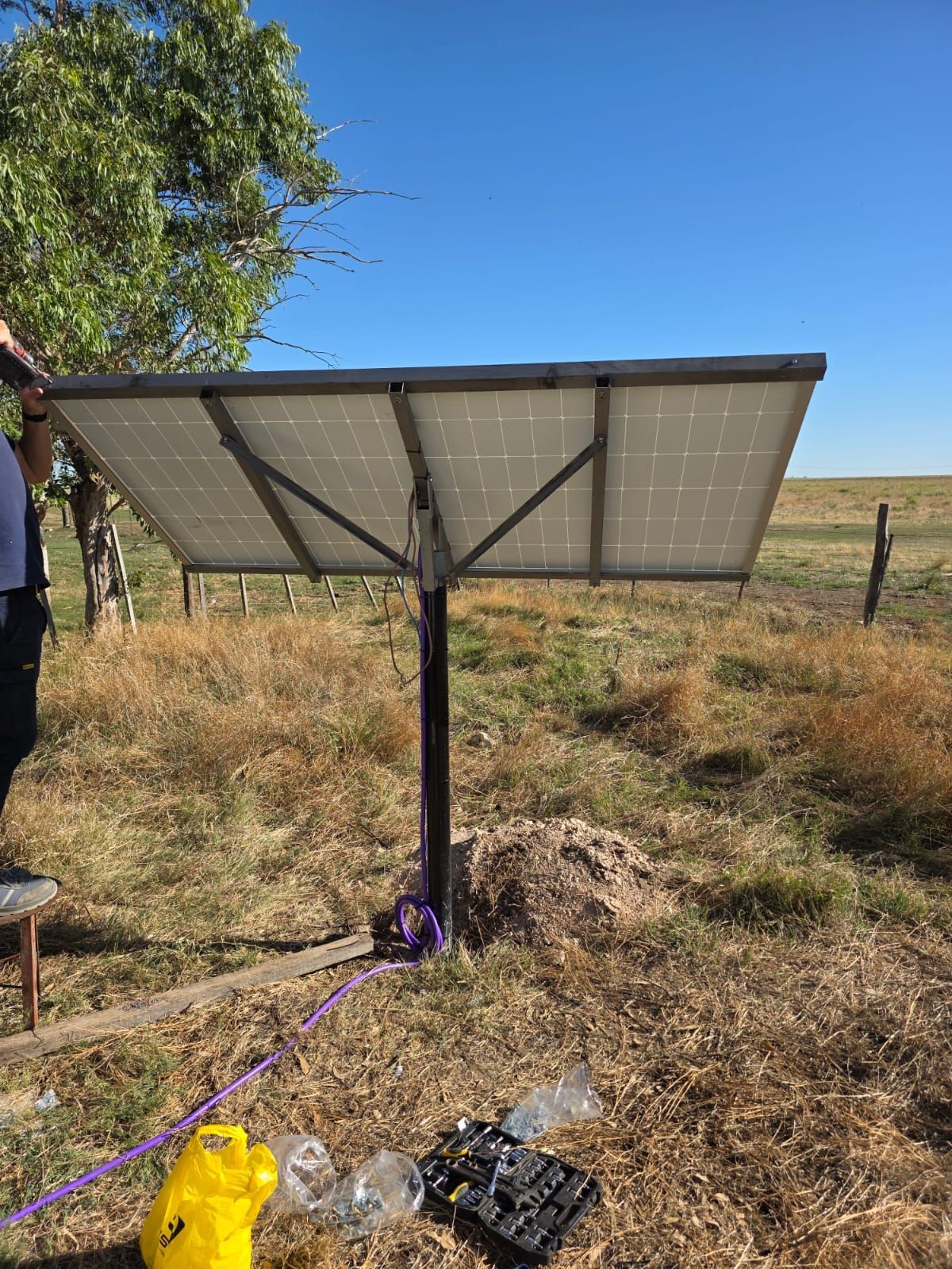 Panel solar en un poste en un campo de hierba en un día soleado. Cables y herramientas en el suelo.