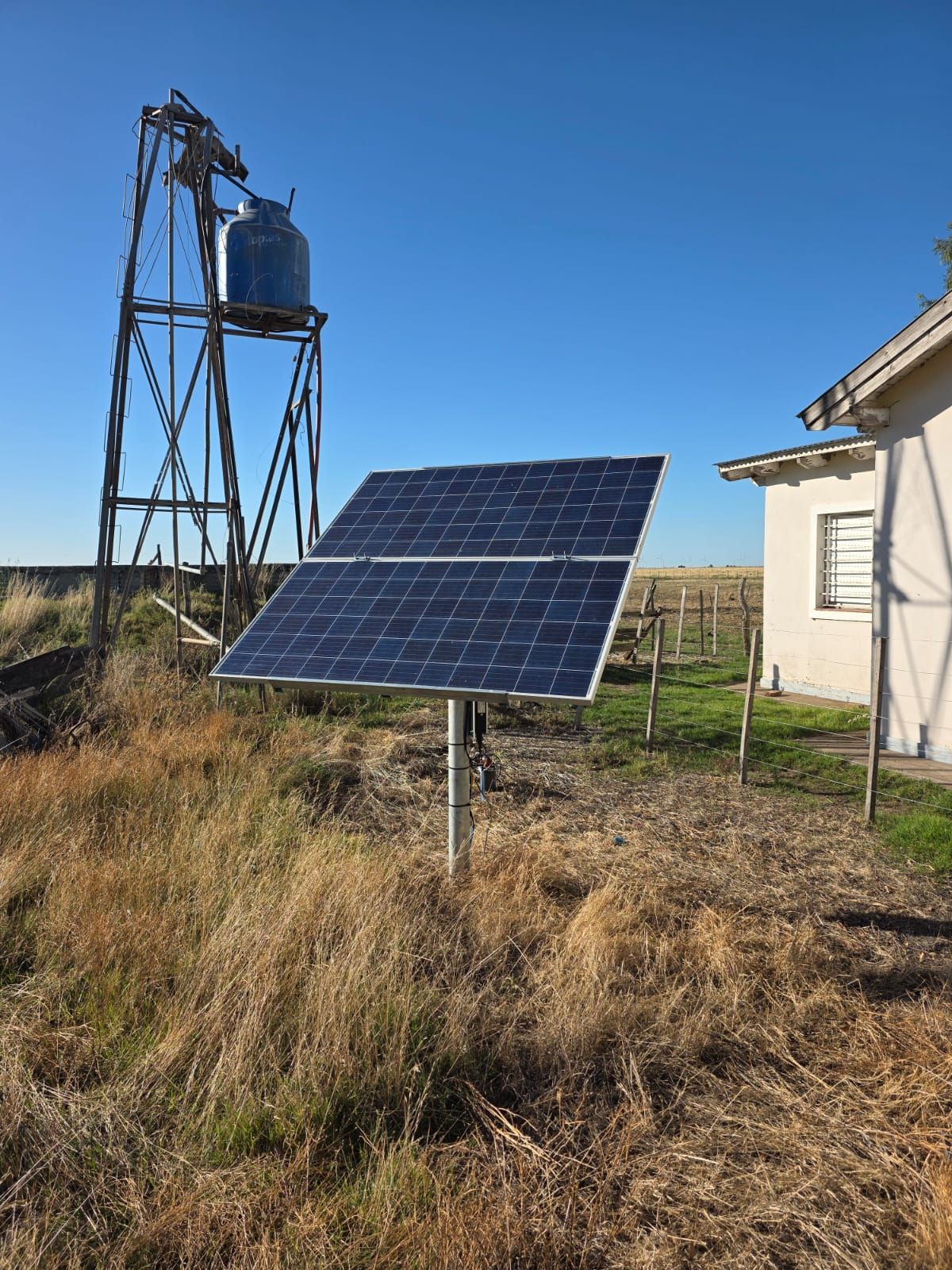 Panel solar en el campo cerca de la torre de agua y el edificio, cielo azul claro.