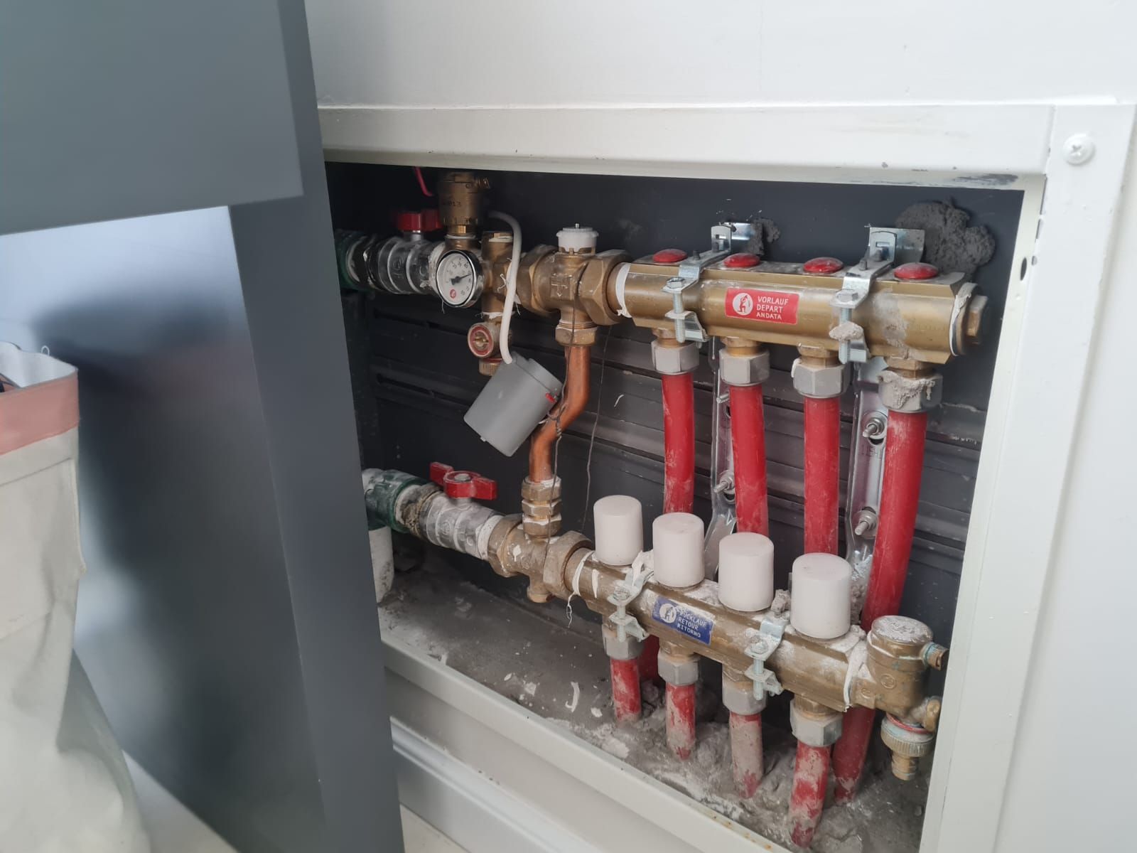 Sistema de tuberías con tubos rojos y de cobre en un nicho de pared blanca. Colectores de latón