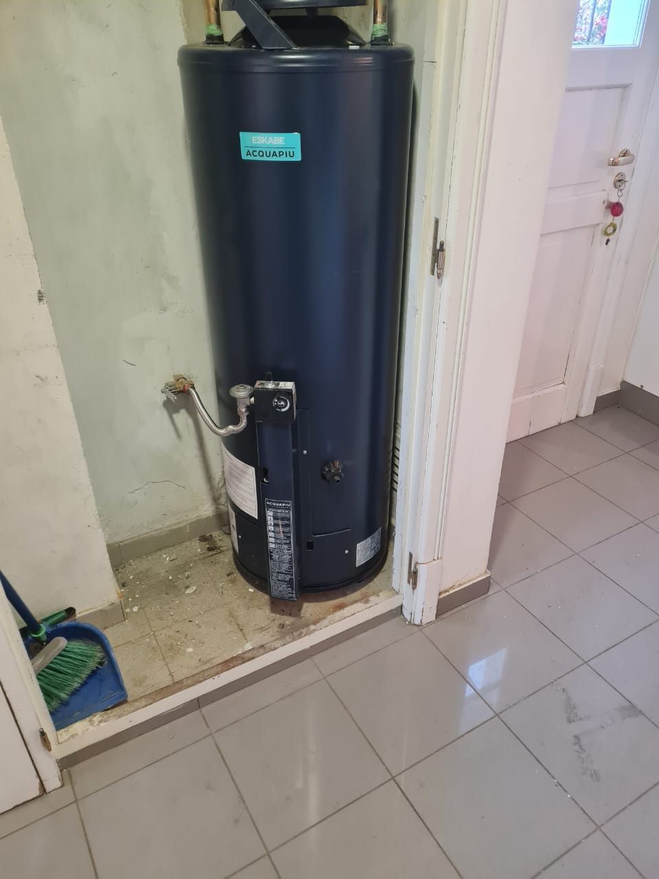 Calentador de agua azul oscuro en un lavadero. Suelo de baldosas grises, paredes y molduras blancas.