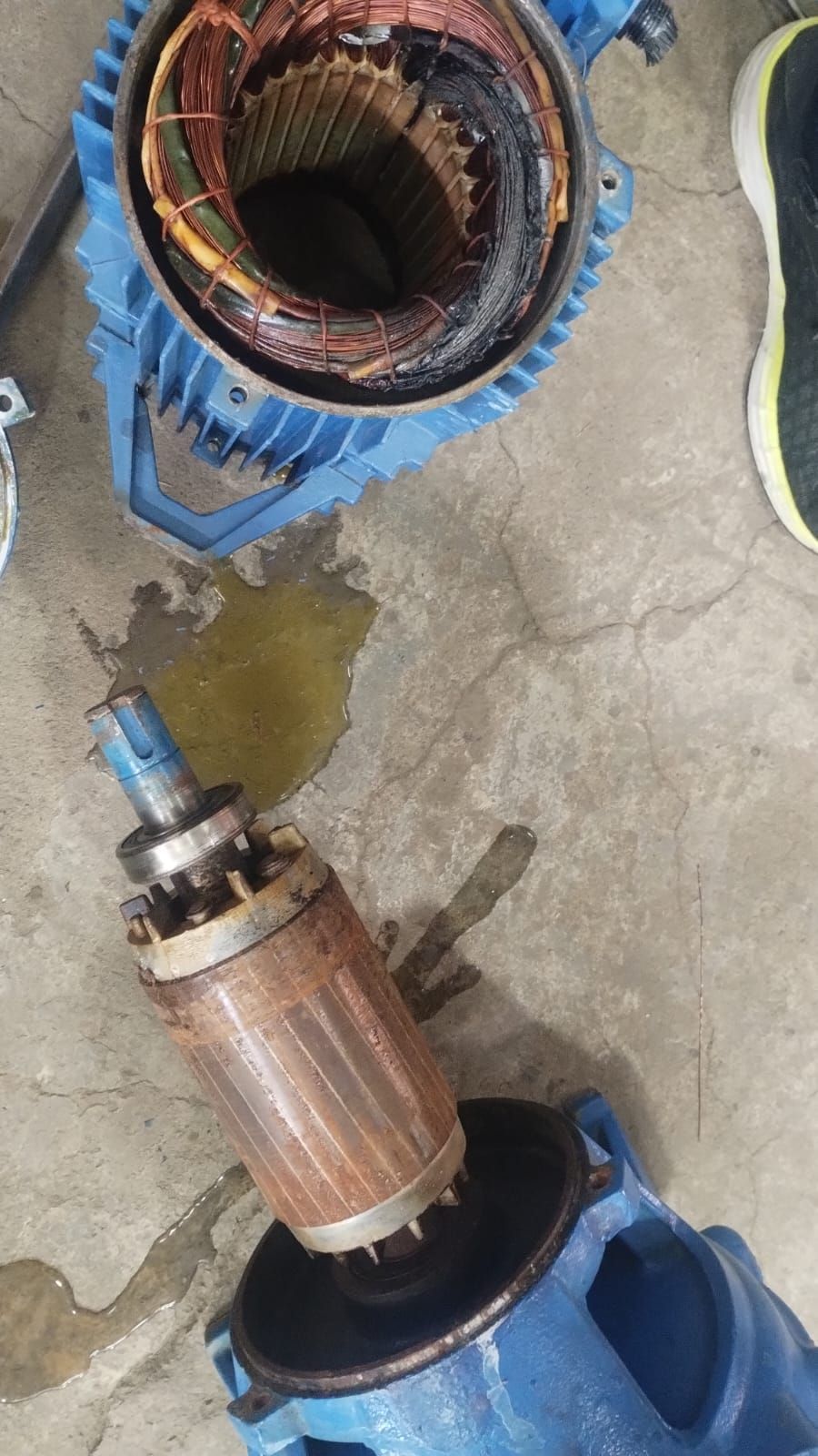 Componentes del motor eléctrico desmontados, incluida la carcasa azul y el rotor oxidado, sobre una superficie de hormigón.