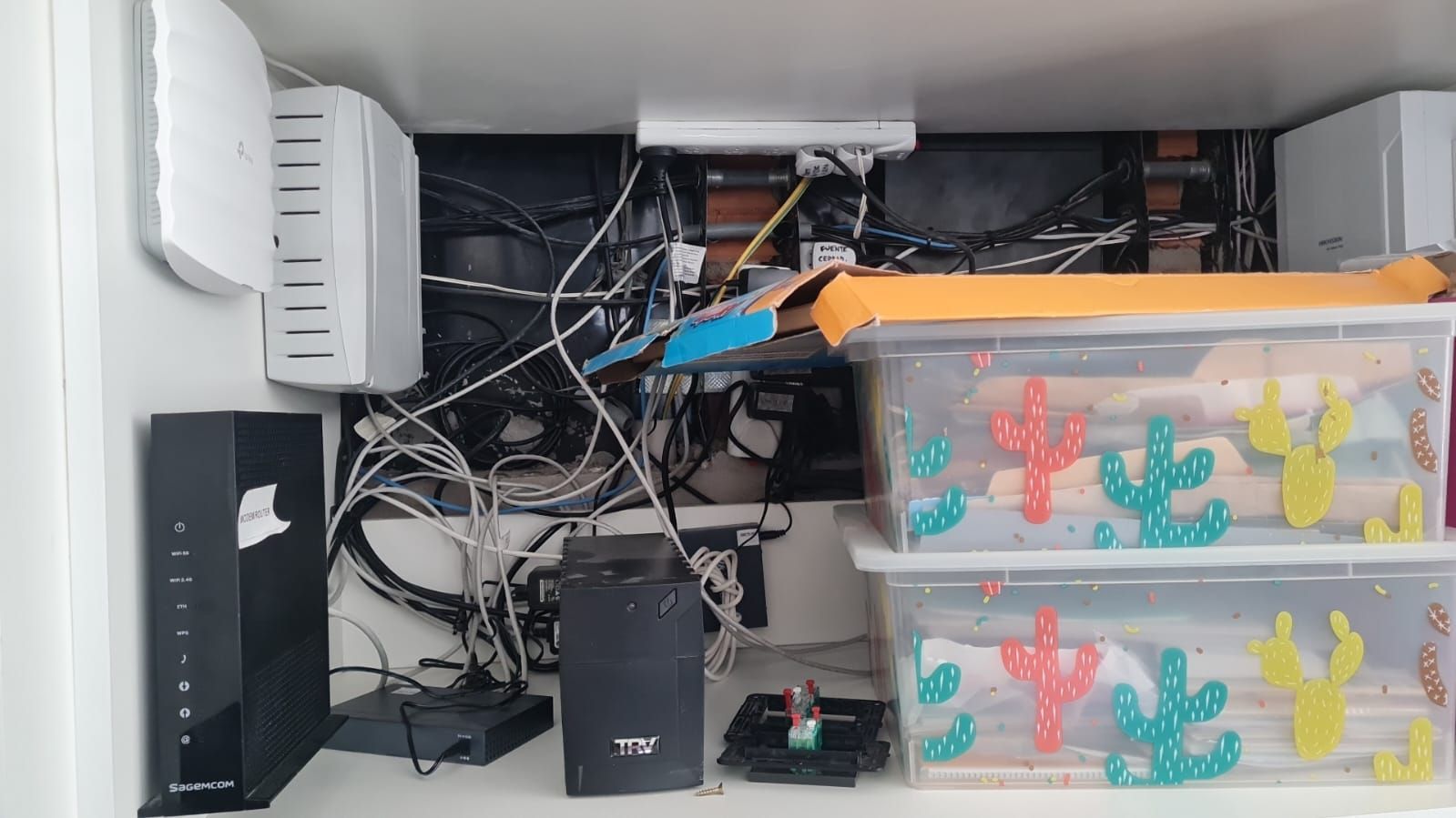 Equipos de red y cajas de almacenamiento en un estante; los cables están enredados.