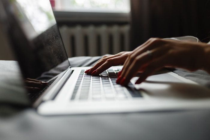 Hands typing on a silver laptop keyboard in a dimly lit, soft-focus setting.