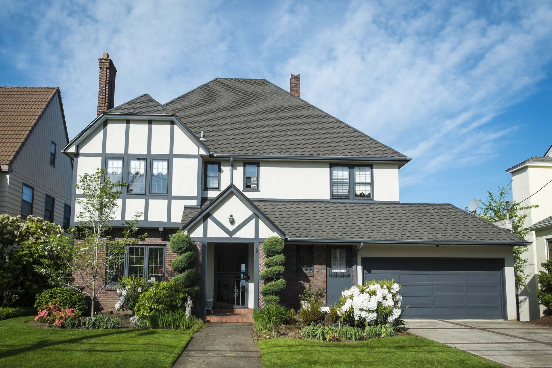 A two-story Tudor-style house with white stucco, dark timber trim, a dark grey roof, and a large attached garage.