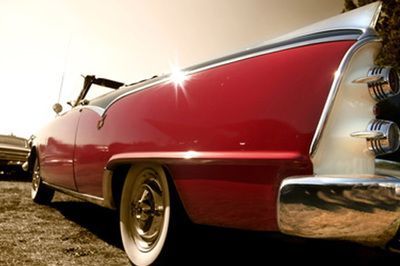 A low-angle view of a red and white vintage convertible car with prominent tail fins parked on a gravel lot.