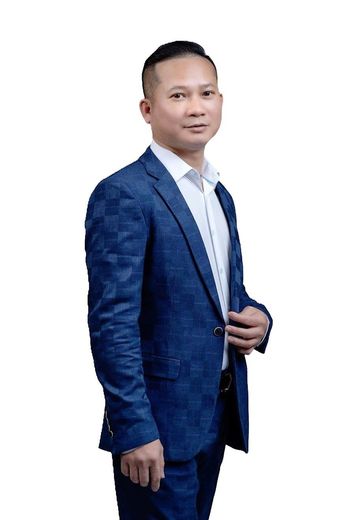 A professional in a blue patterned suit and white shirt, standing against a white background.