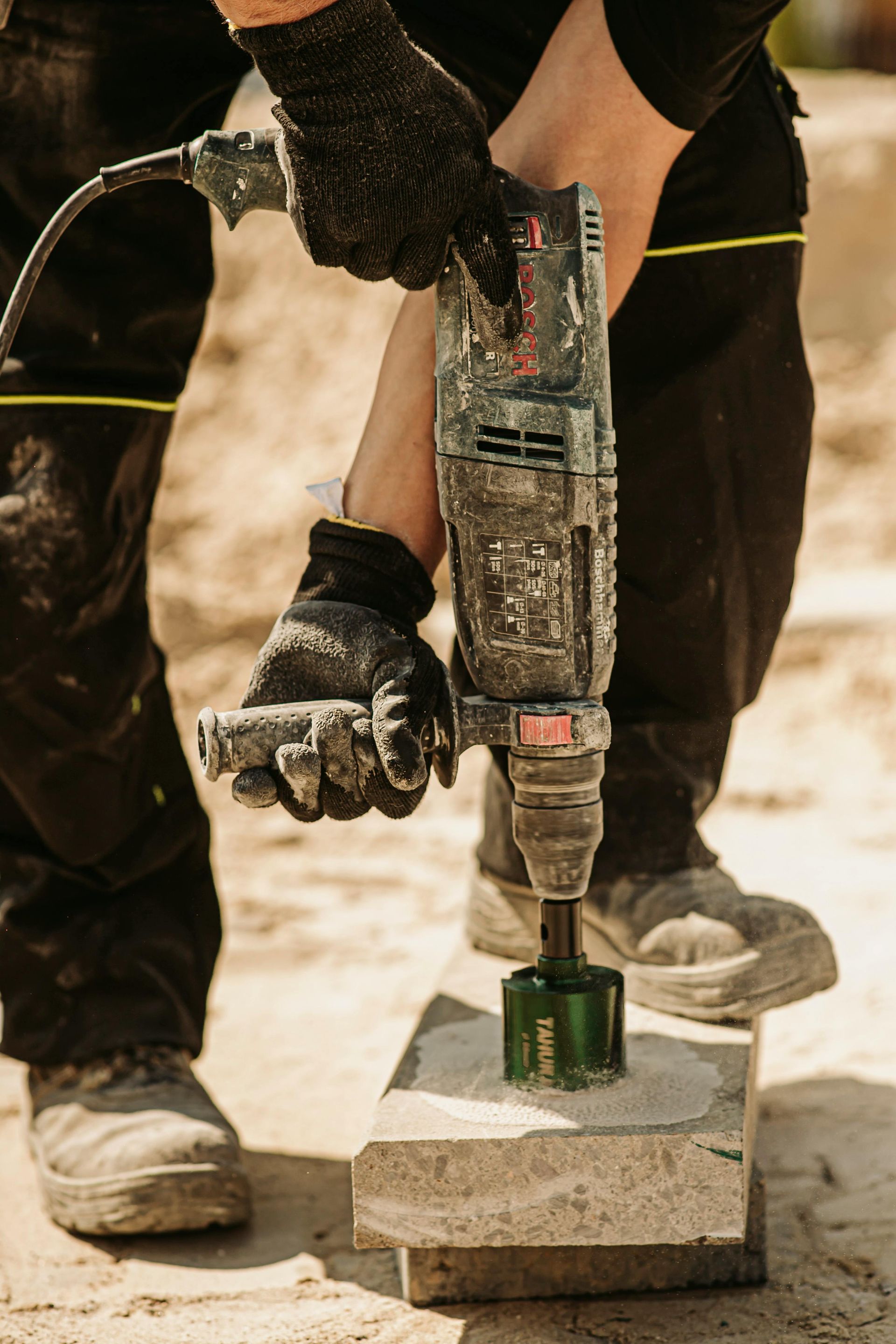Person wearing gloves using a power drill to make a hole in a stone block.