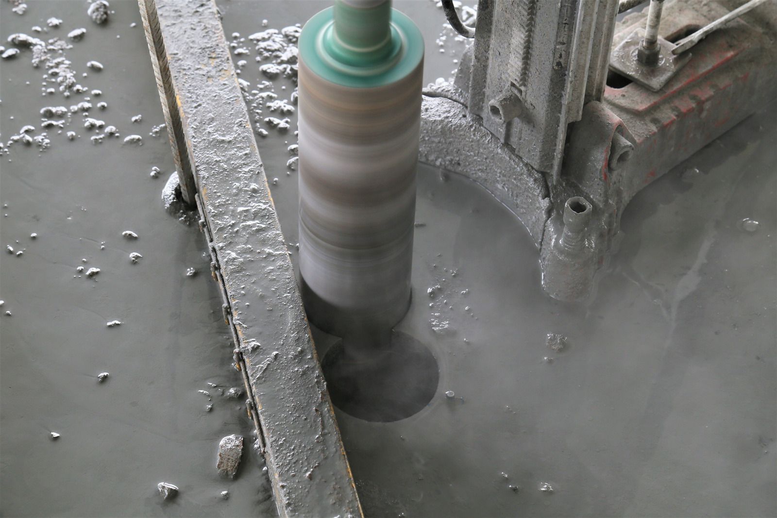 A core drilling machine drilling a hole in concrete; water and debris visible.