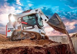 White skid-steer loader dumping dirt at a construction site under a cloudy sky