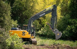 Yellow excavator digging in a wooded area beside a dirt path
