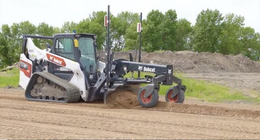White compact track loader pulling a black soil grader on a dirt lot
