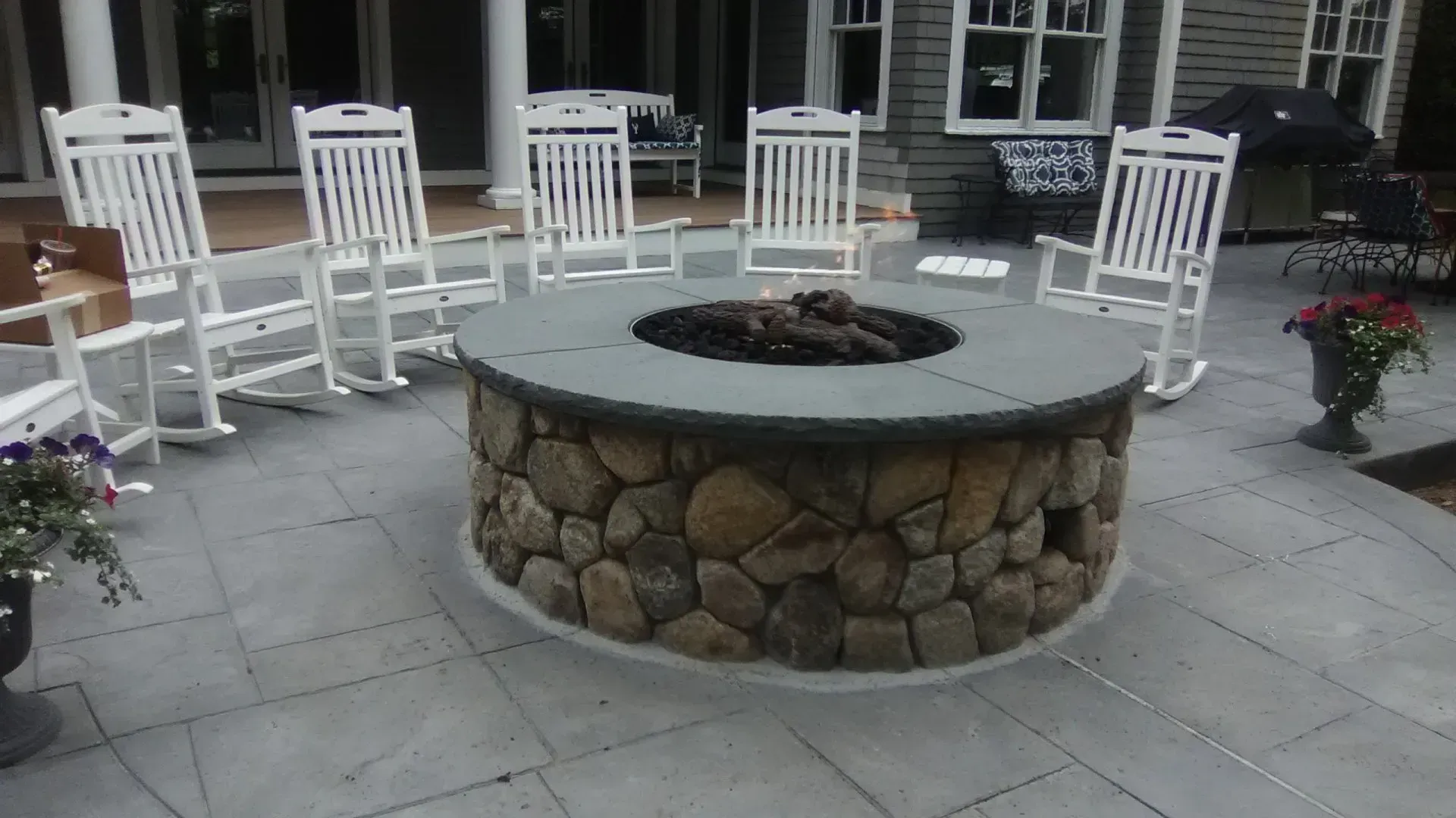 a fire pit on a patio with rocking chairs around it