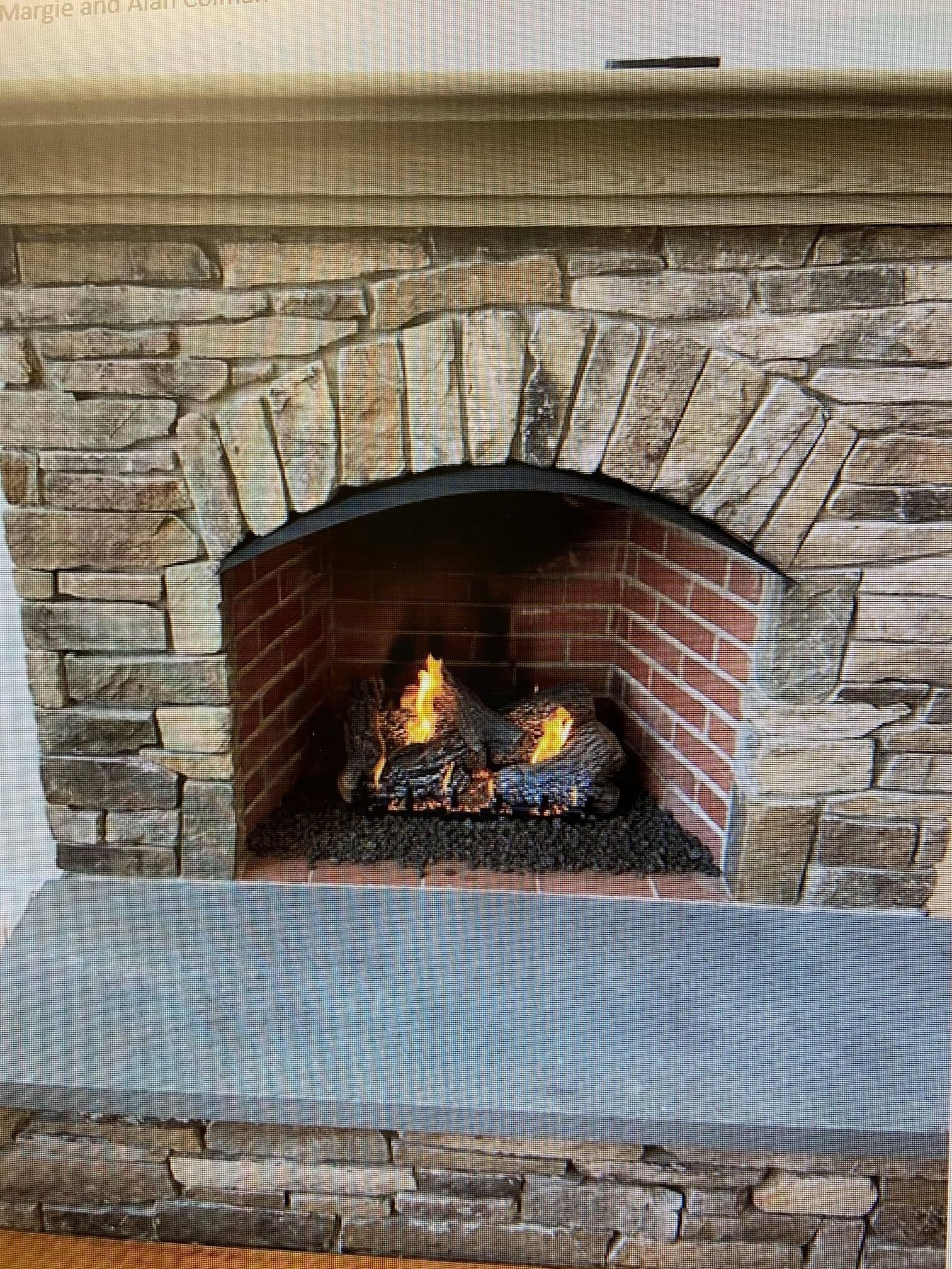 A brick fireplace with a stone wall and a fire in it.