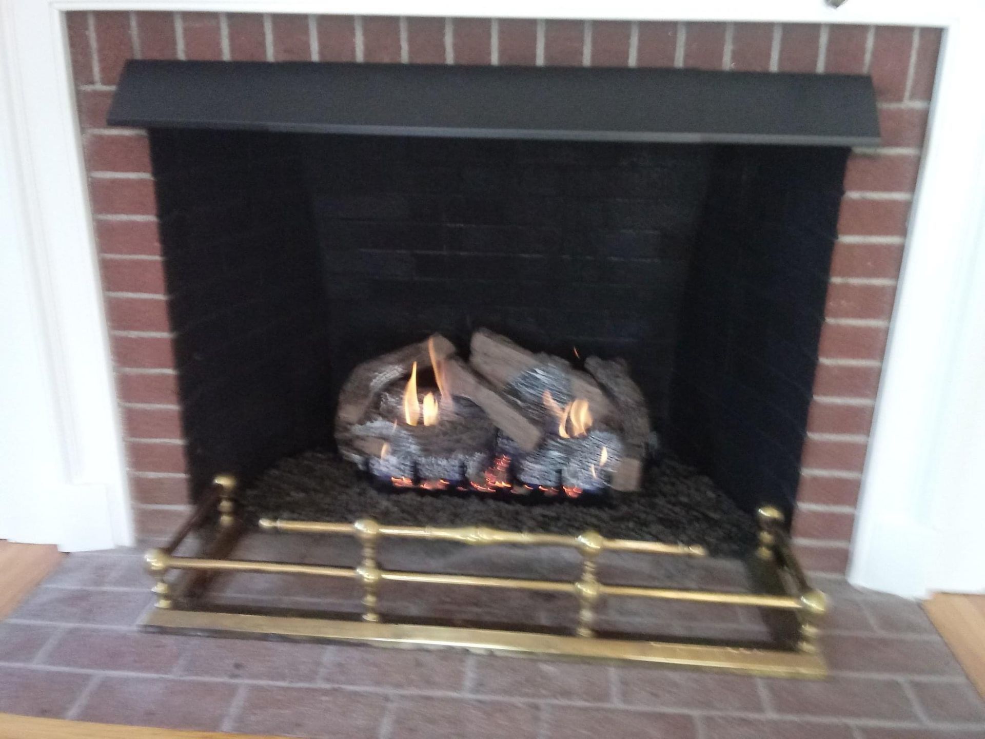 A brick fireplace with a black hood and a brass grate