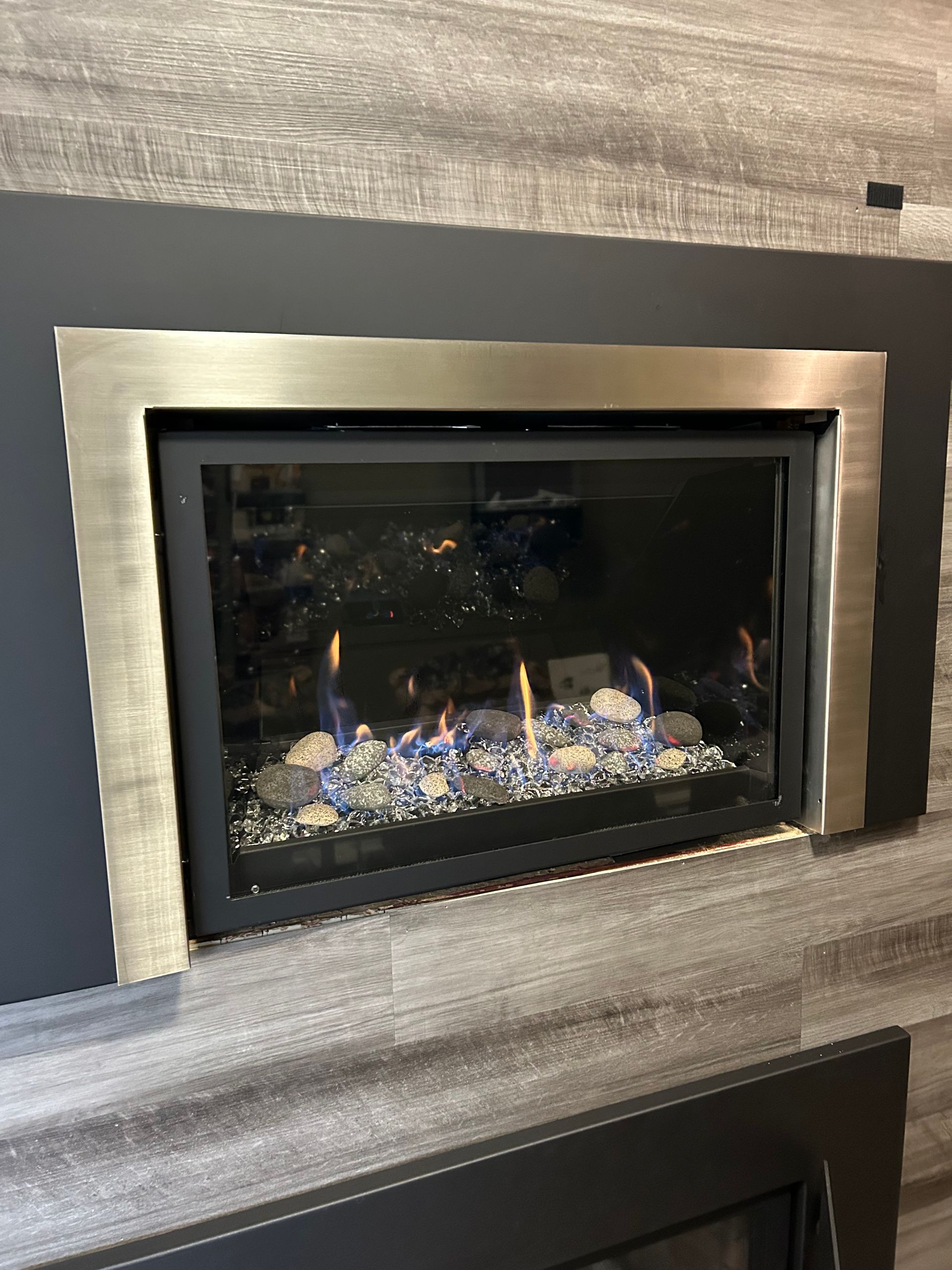 A fireplace with a stainless steel frame and glass rocks in it.