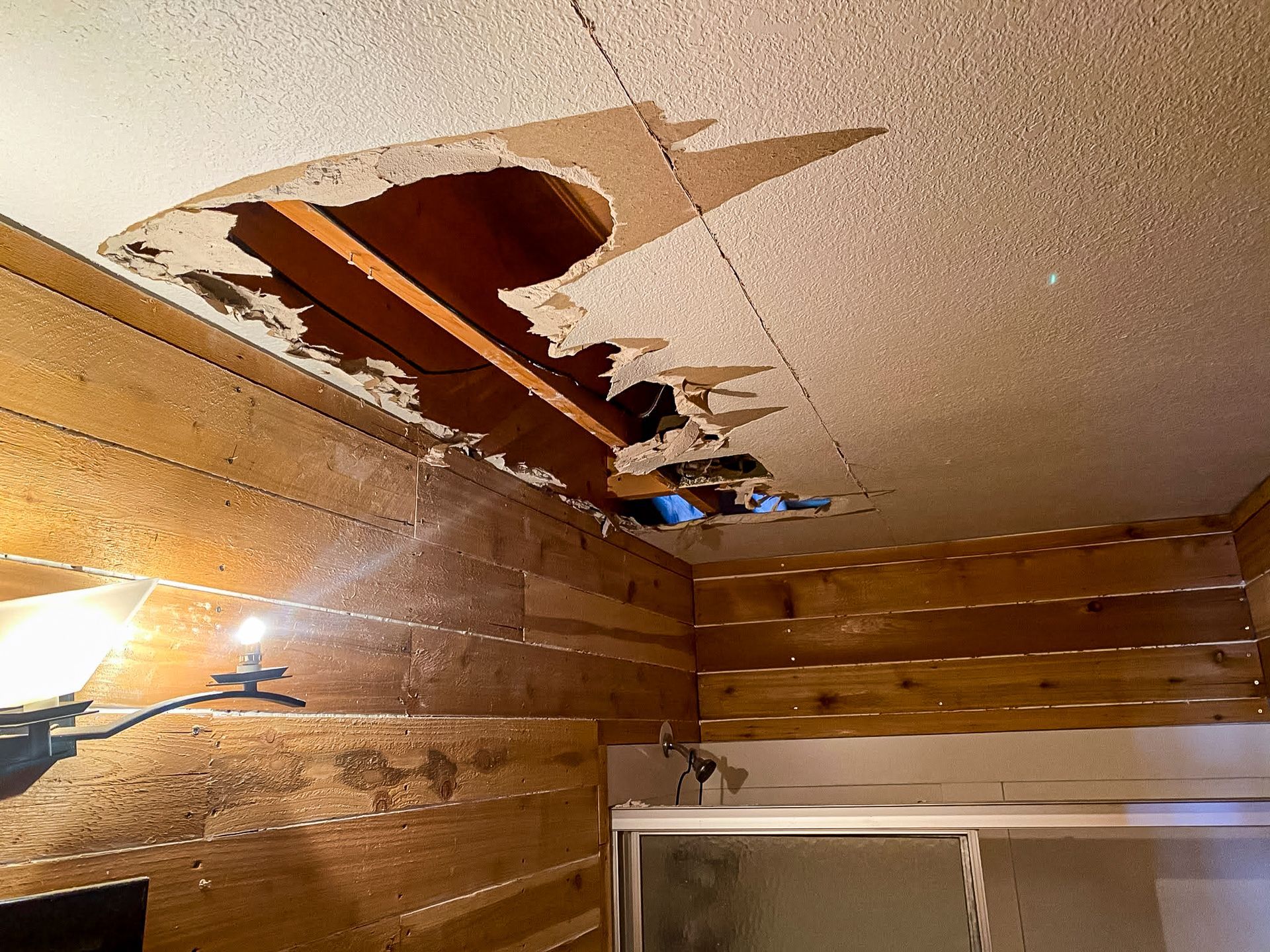 A bathroom with a hole in the ceiling and wooden walls.